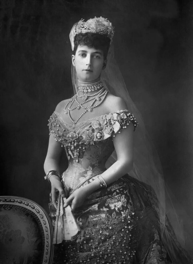 Queen Alexandra of England wearing a tight corset and crinoline dress adorned with numerous elaborate jewels